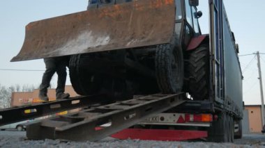 Traktör kazıcısı uzun bir kamyon platformuna düştü