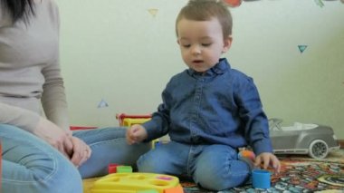 Bir çocuk yerde oturan anne oyuncaklarıyla oynuyor.