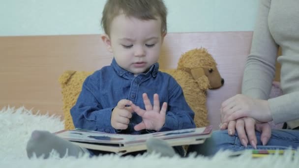 Un bambino legge libri accanto alla mamma seduta su un divano — Video Stock
