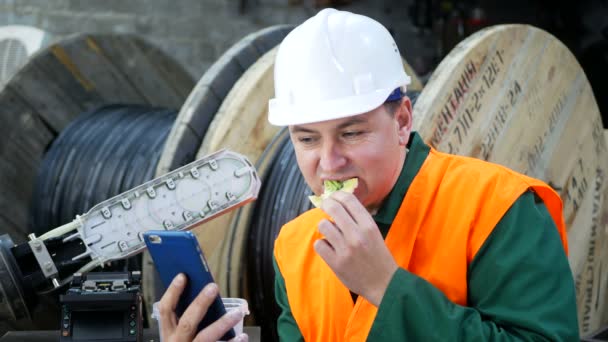 Μηχανικός τρώει στο χώρο εργασίας με ένα τηλέφωνο στα χέρια του — Αρχείο Βίντεο