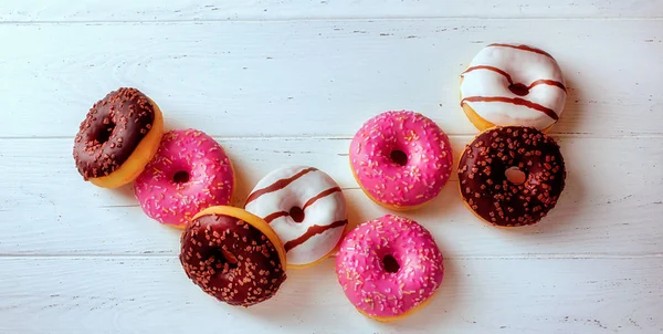 Top view of assorted doughnuts, on a white wooden background, wi