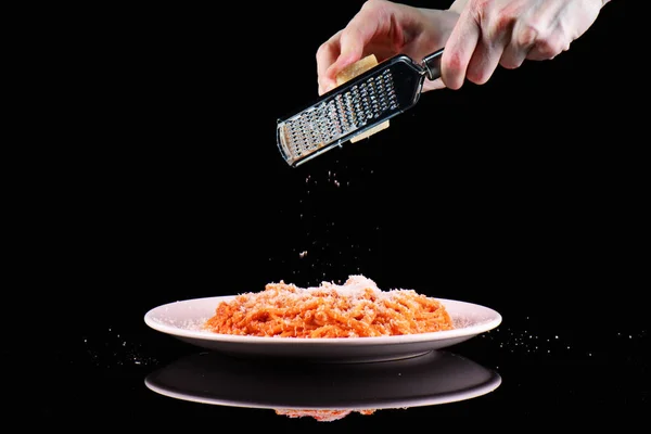 Strofinare il parmigiano grattugiato sul piatto di pasta. Mani grattugiare formaggio su sfondo nero . — Foto Stock