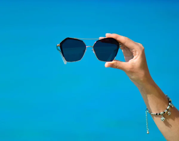 Mujer mano celebración gafas de sol en tropical playa mar — Foto de Stock