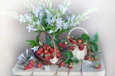 Beyaz çiçek buketi ve hasır sepet içinde olgun çilek.