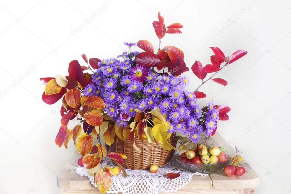 Still life with autumn leaves and flowers in a basket on a white background in the room.
