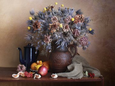 Vazoda bir buket kurumuş çiçek ve masada meyve. .