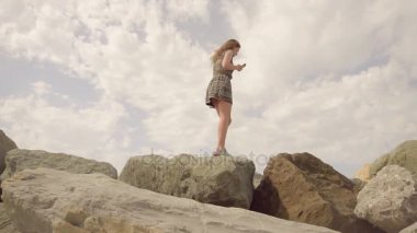 Bir cep telefonu onun elinde tutan dar bir tepede Dengeleme denizin kayalık sahil kız yürüyor. Ağır çekim