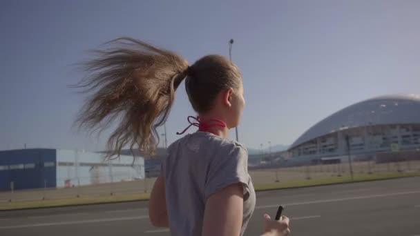 Een jong meisje in de vroege ochtend joggen. Op de achtergrond, sportfaciliteiten in Sotsji stad — Stockvideo