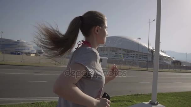 Uma rapariga a correr de manhã cedo. No fundo, instalações desportivas na cidade de Sochi — Vídeo de Stock