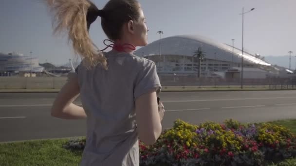 Una joven corriendo por la mañana temprano. En el fondo, instalaciones deportivas en la ciudad de Sochi — Vídeos de Stock