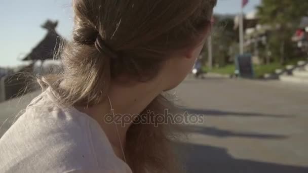 Porträtt av en flicka utomhus med sin smartphone, i bakgrunden passerar cyklister — Stockvideo
