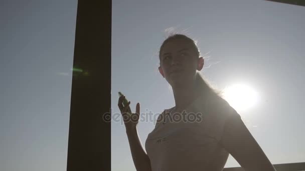 Ein Mädchen mit ihrem Smartphone blickt in die Sonne — Stockvideo