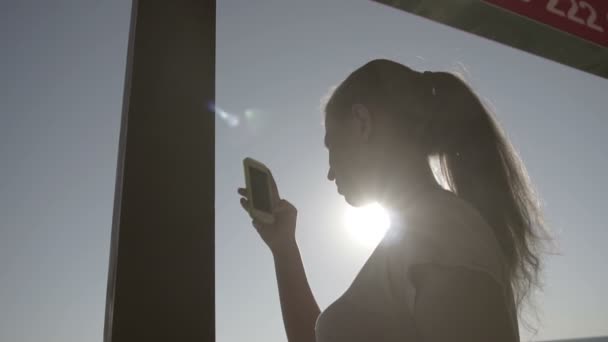 En tjej med hennes smartphone ser på solen — Stockvideo