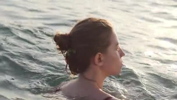 Portrait d'une jolie jeune femme nageant dans la mer au coucher du soleil, surface lisse, Gros plan — Video