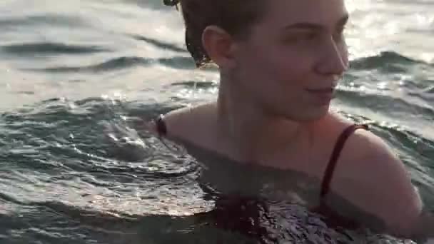 Portré egy vonzó fiatal nő úszik a tengerben naplementekor, sima felület, közelkép — Stock videók