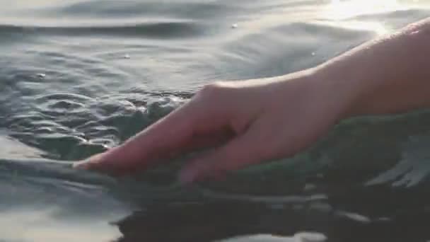 Kvinnlig hand lekfullt och försiktigt vidrör havsytan i bländning av solen vid solnedgången, Närbild, — Stockvideo