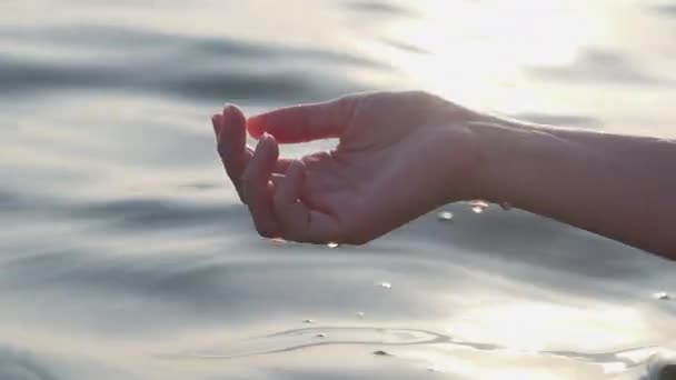 Жіноча рука торкається, грає з морською водою в сяйві сонця на заході сонця, Крупним планом — стокове відео