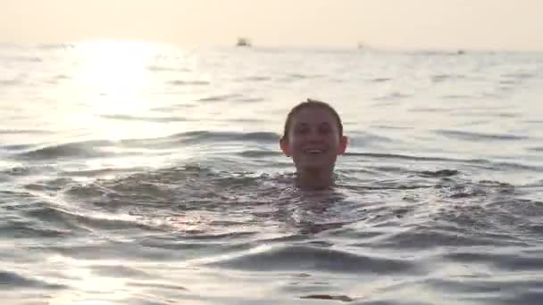 Jovem brincalhão nada no mar sorrindo e dabbling, luz de fundo, pôr do sol — Vídeo de Stock