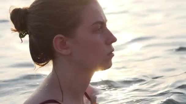 Egy fiatal lány úszik a tengerben komoly és elmélkedő arckifejezéssel. — Stock videók