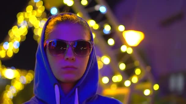 Een meisje in een blauwe hoodie staat in de neon lichten van een grote stad — Stockvideo