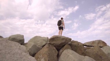 Bir adam dağın tepesinde muzaffer bir şekilde duruyor ellerini kaldırıyor, ağır çekimde.