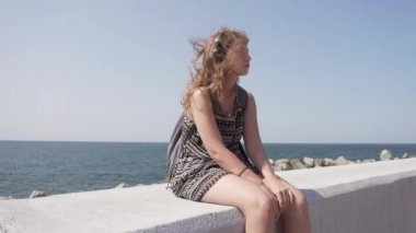 Sırt çantası ve kulaklığı olan bir kız gezinti güvertesinde oturuyor.