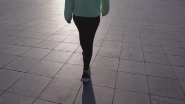 Gün batımında şehir caddesinde yürüyen eşofmanlı bir kız.