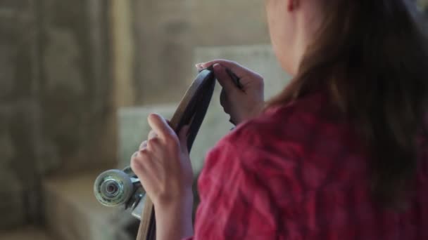 Chica joven con un monopatín en un taller — Vídeo de stock