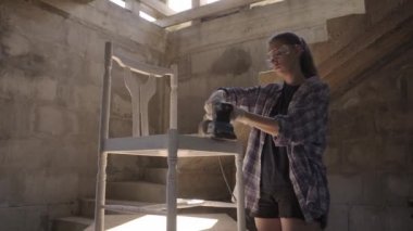 Kız marangoz zımpara makinesi kullanarak antika mobilyaları tamir ediyor.