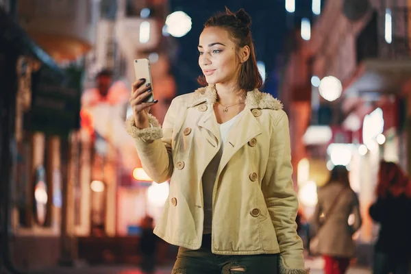 Девушка проверяет свой телефон на улице ночью — стоковое фото