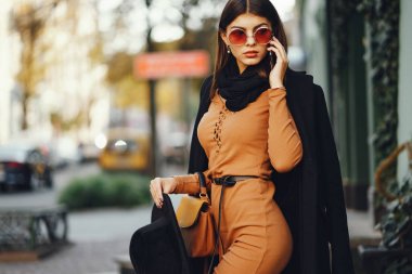 Şık bir kız telefonunu kullanarak şehirde dolaşıyor.