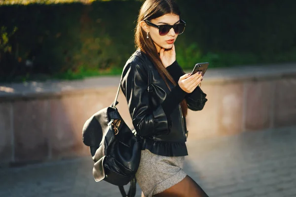 一个时髦的女孩一边用电话在城市里走来走去 — 图库照片
