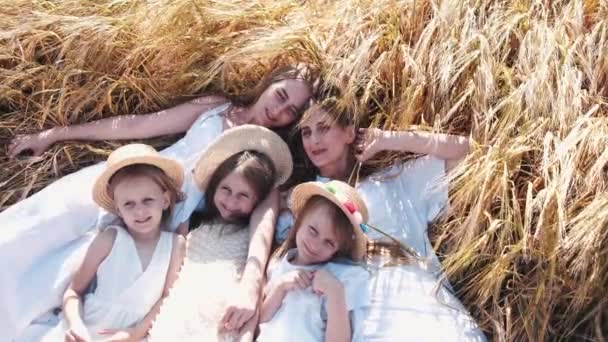 Три дівчинки в сукнях лежать на пшеничному полі з матерями — стокове відео