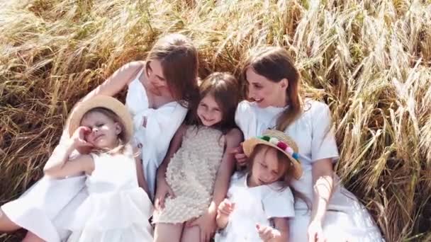 Три маленькие девочки в платьях лежат на пшеничном поле с матерями — стоковое видео