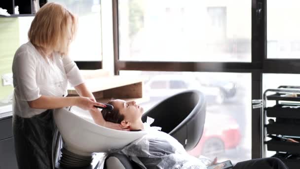 Friseur mit blonden Haaren wäscht Kunden den Kopf im Waschbecken — Stockvideo