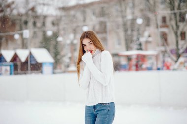 Kış parkında duran beyaz kazaklı genç kız.