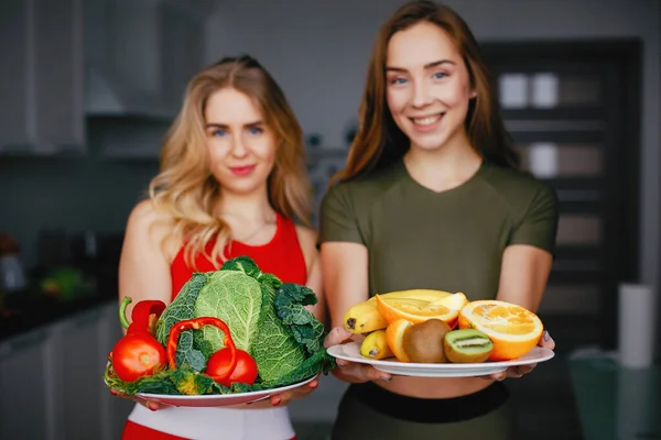 Zwei Sportlerinnen in einer Küche mit Gemüse — Stockfoto