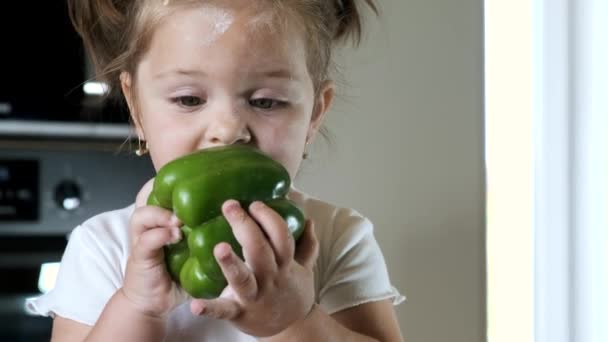 Πορτρέτο του κοριτσιού δάγκωμα πράσινο πιπέρι στη σύγχρονη κουζίνα — Αρχείο Βίντεο