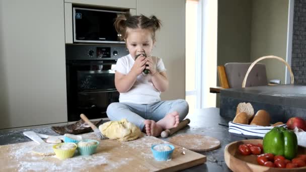 Mała dziewczynka w białym T-shirt siedzi na stole w kuchni — Wideo stockowe