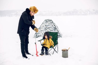 Kışın oğluyla balığa çıkan yakışıklı bir adam.