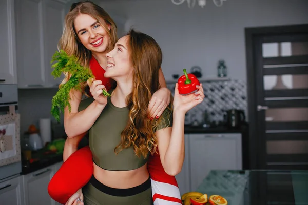 Twee sporten meisje in een keuken met groenten — Stockfoto