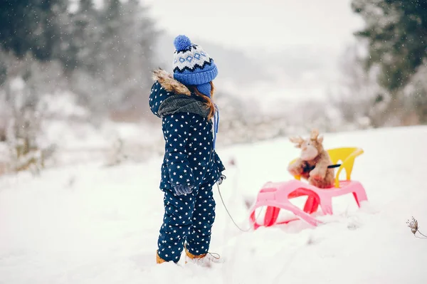 Mała dziewczynka w niebieskim kapeluszu bawiąca się w zimowym lesie — Zdjęcie stockowe