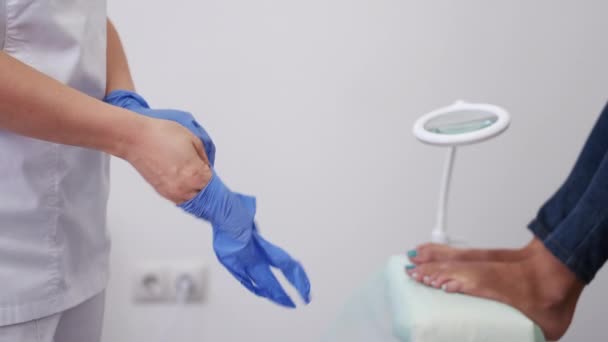 The pedicure technician is putting on rubber gloves before the procedure — Stock Video