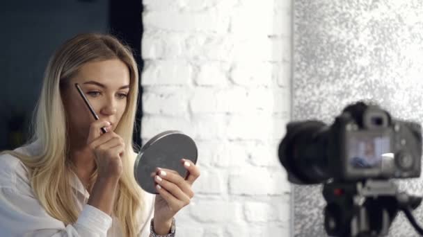 Η όμορφη vlogger ζωγραφίζει τα φρύδια της στην κάμερα με έναν καθρέφτη. — Αρχείο Βίντεο