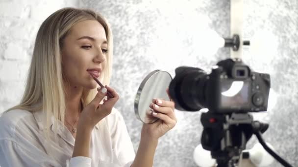 Eine hübsche Visagistin trägt Lippenstift auf ihre Lippen auf und schaut in einen Spiegel — Stockvideo