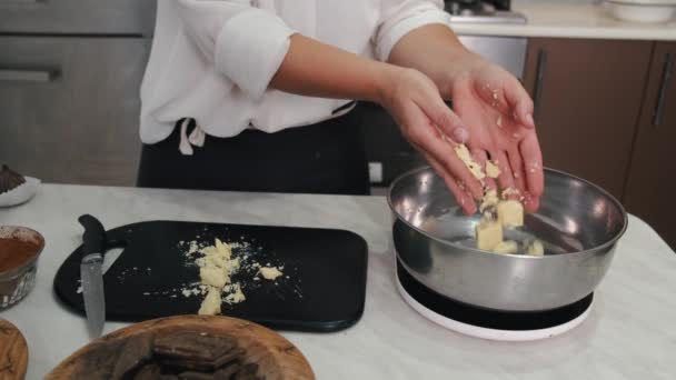 De vrouw gooit chocoladestukjes in een kom. — Stockvideo