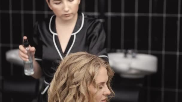 Cabeleireiro em preto uniforme curling cabelo loiro no salão — Vídeo de Stock