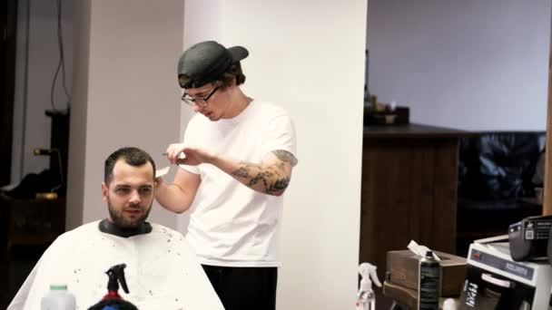 Peluquero en gorra negra haciendo peinado para cliente en barbería — Vídeos de Stock