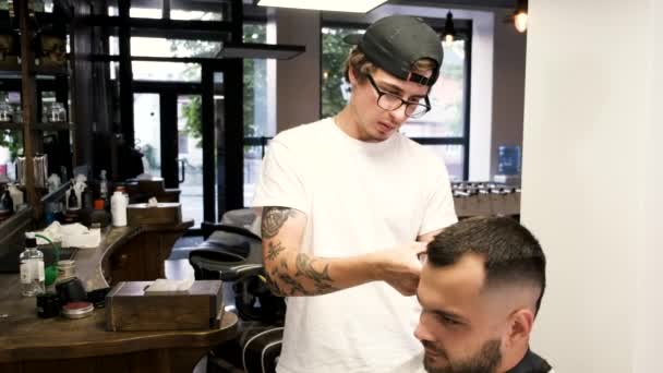 Barber doing stylish hairstyle for client in barber shop — Stock Video