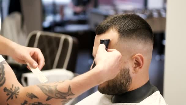Fryzjer robi fryzurę dla brodatego mężczyzny w salonie fryzjerskim — Wideo stockowe
